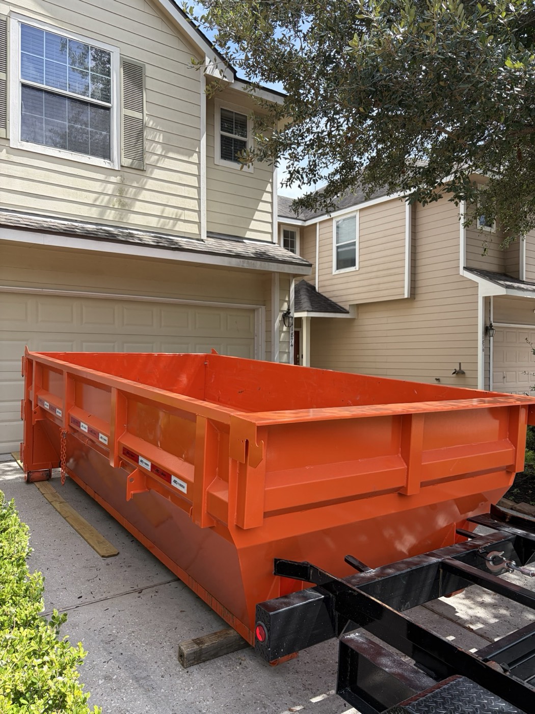 Empty orange 14-yard roll-off can on a clean townhome driveway under an oak