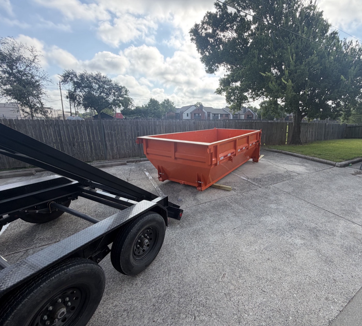Empty roll-off can and trailer parked on a back driveway