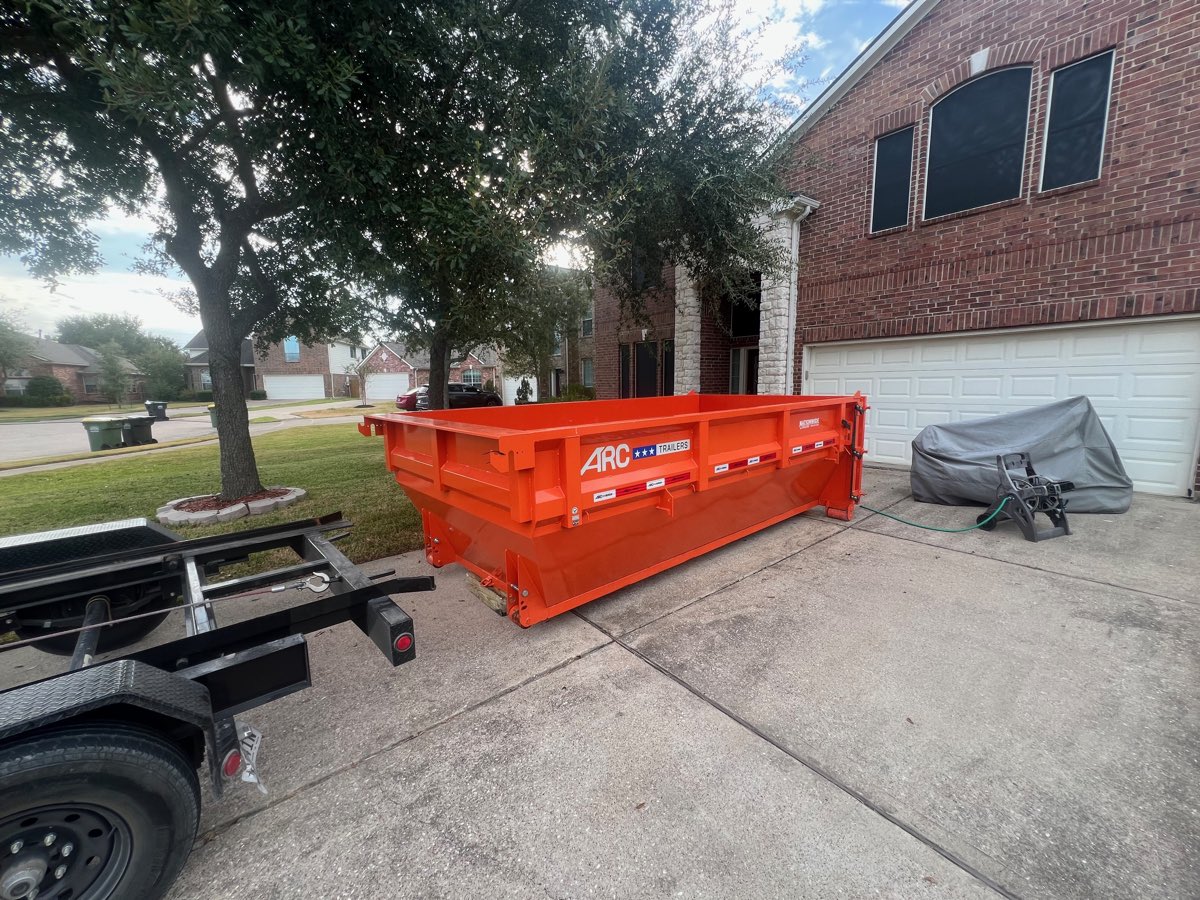 Roll-off dumpster on a residential driveway beside a two-car garage