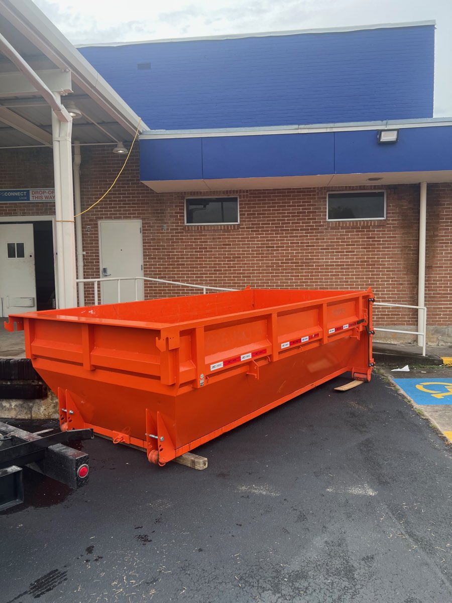 Orange roll-off dumpster on asphalt outside a commercial building