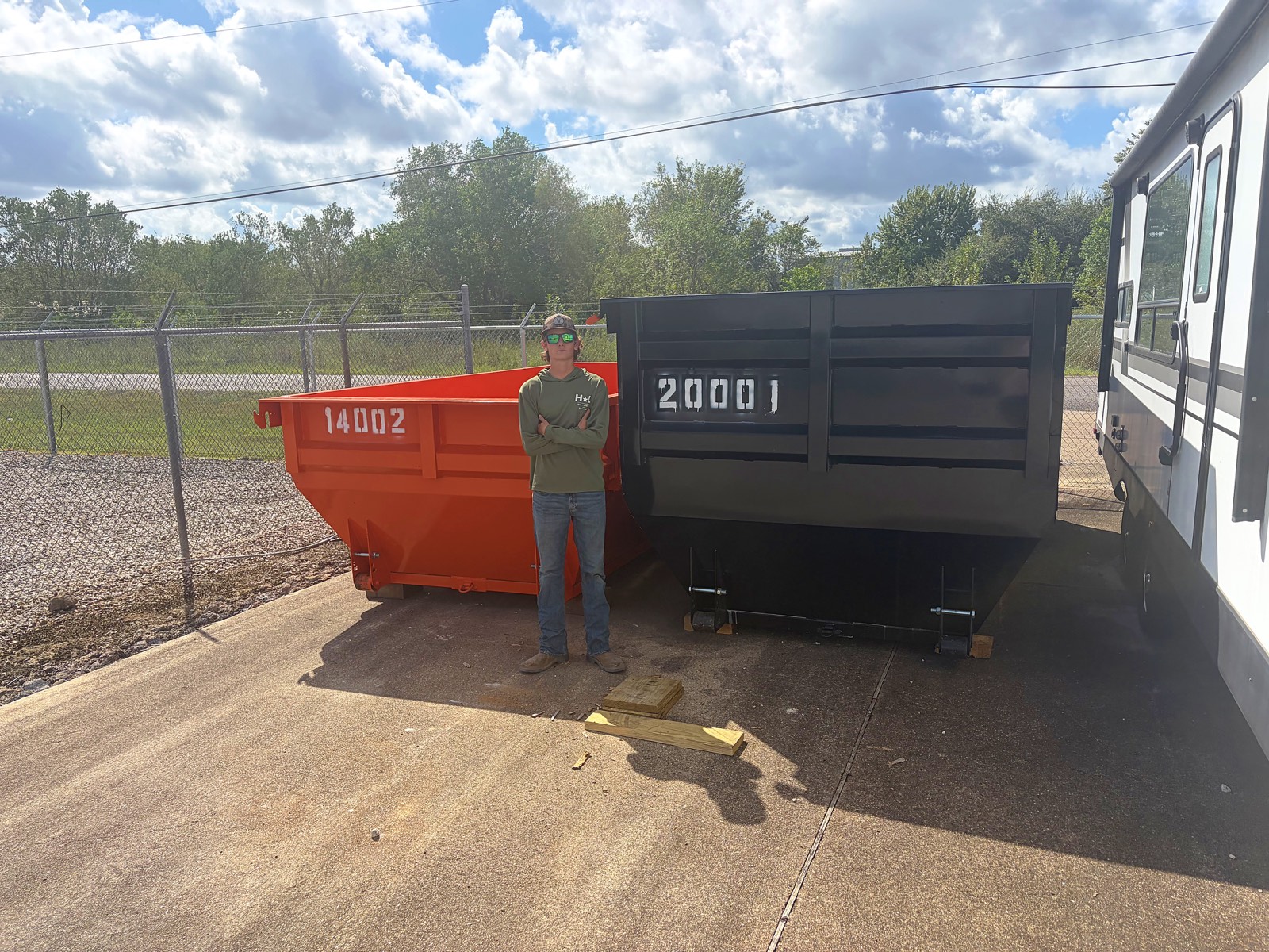 Hayden, uno de los dueños de H&L, parado entre el dumpster naranja de 14 yardas y el negro de 20 yardas en nuestro patio de Pearland
